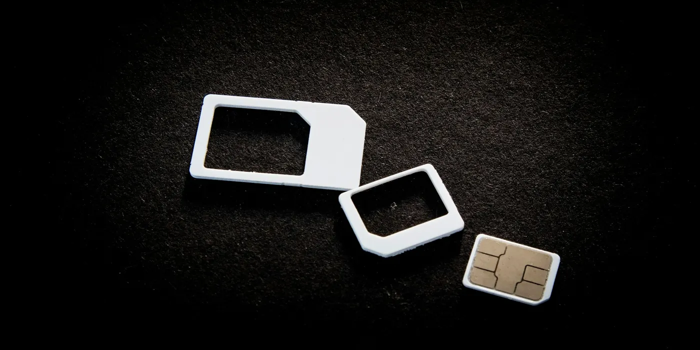 A physical SIM card and adapters on a dark surface