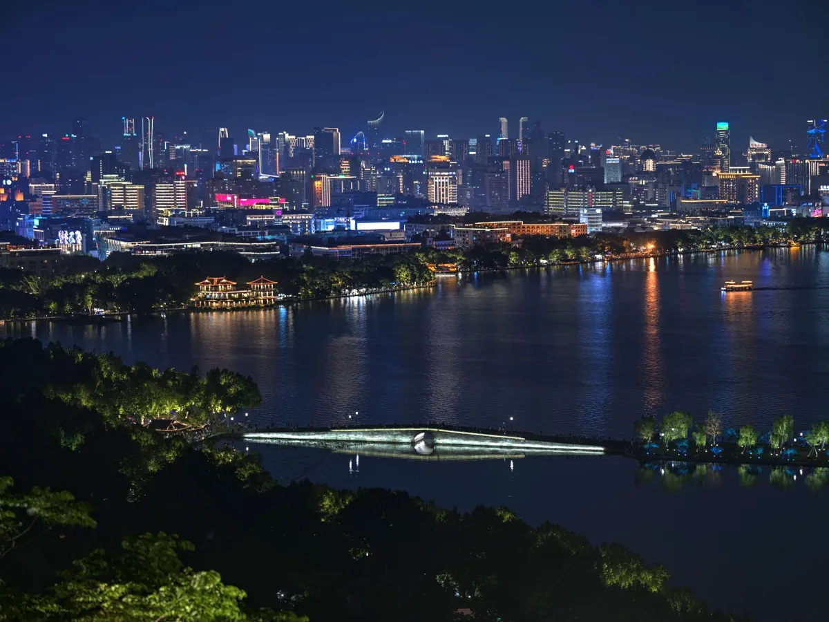 West Lake at night with the lit Hangzhou skyline across the water