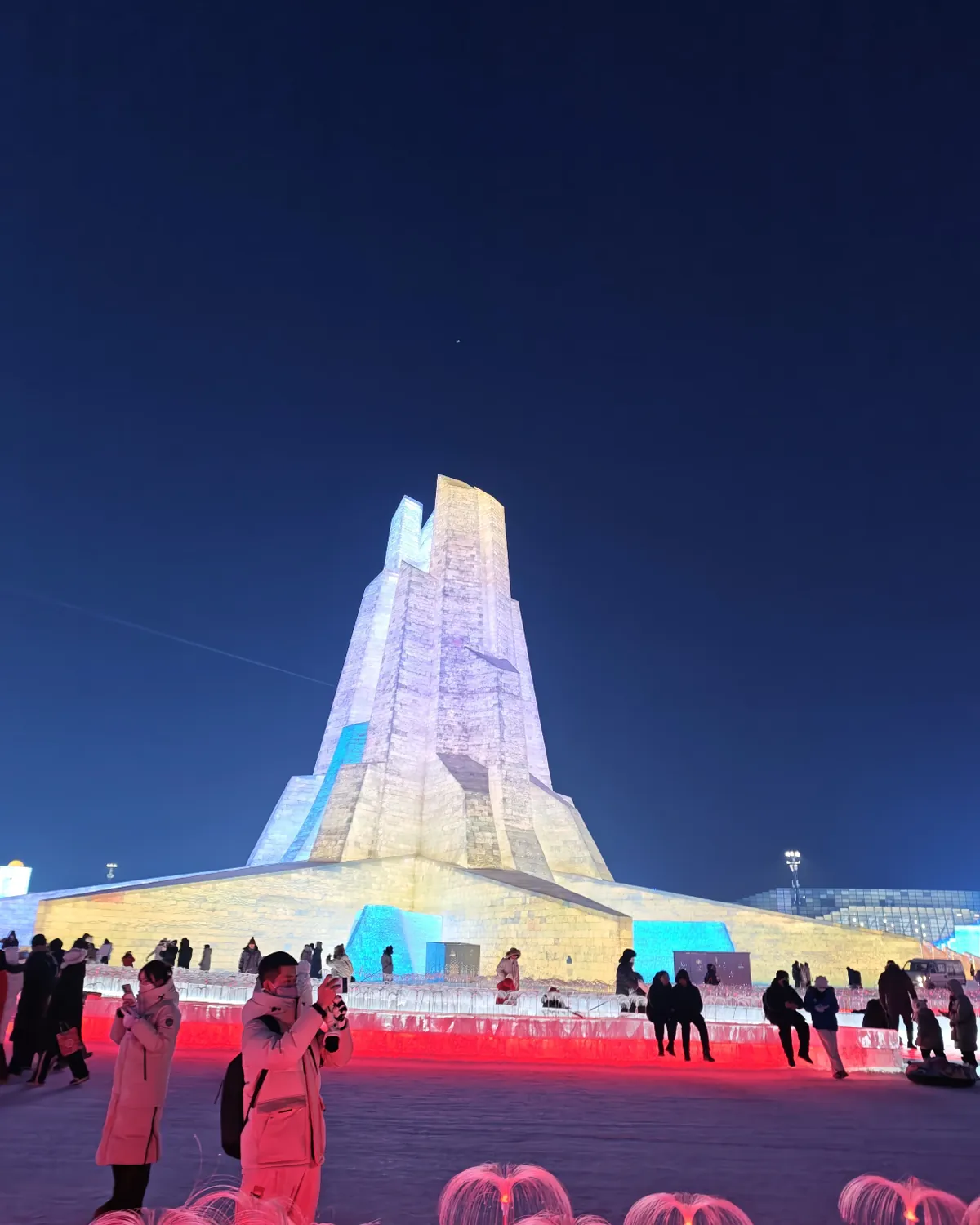 Tall illuminated ice tower at night inside Harbin Ice and Snow World