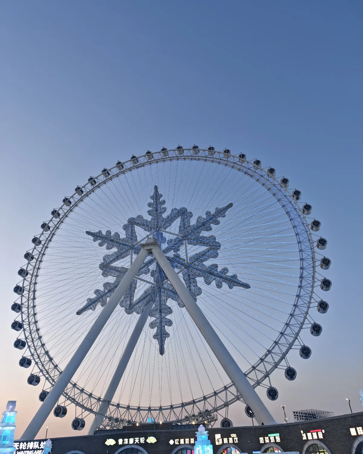 Snowflake-shaped Ferris wheel above ice buildings at Harbin Ice and Snow World