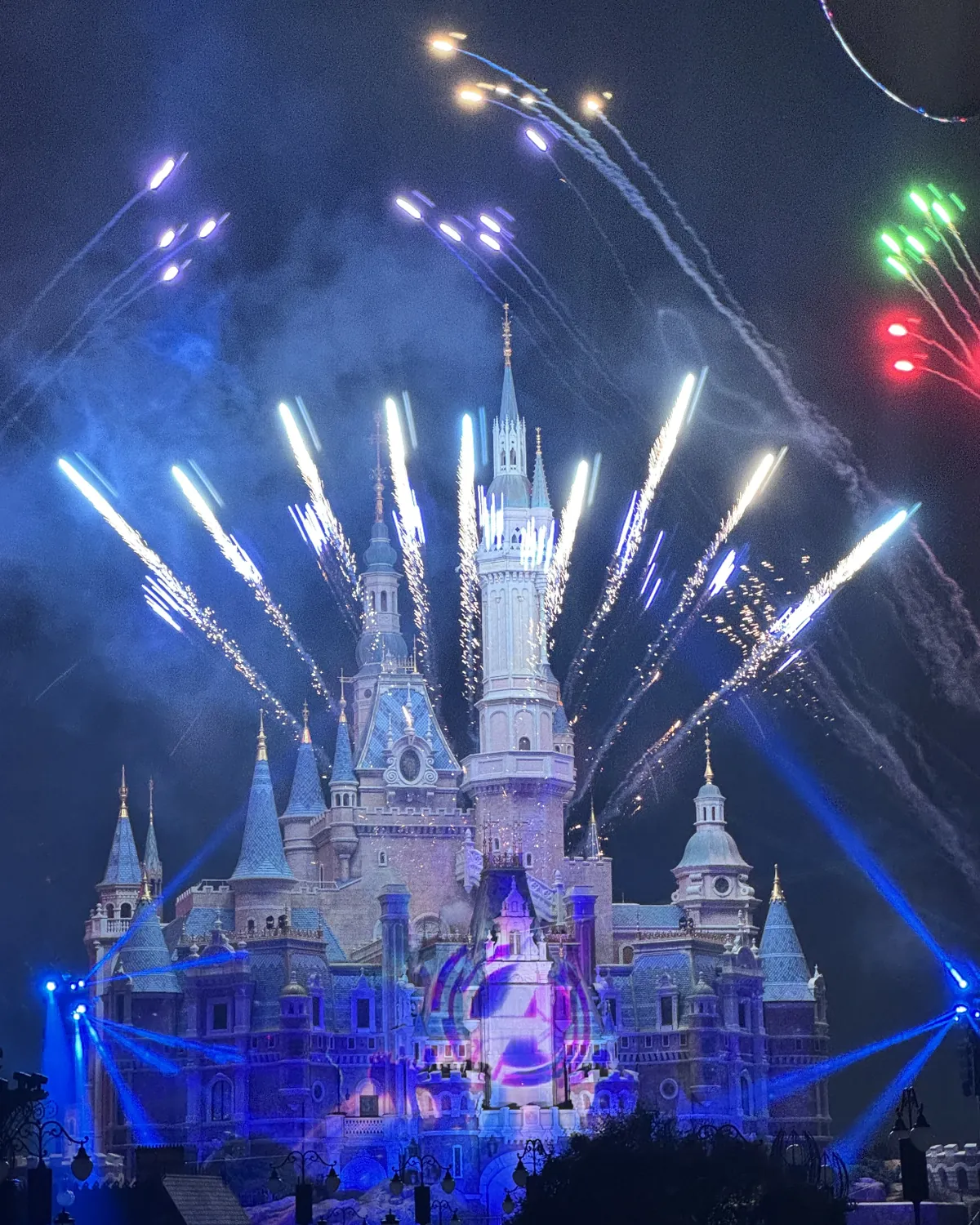 The castle lit blue during the nighttime fireworks show at Shanghai Disneyland; the show ends late, so plan the ride back or sleep near the resort