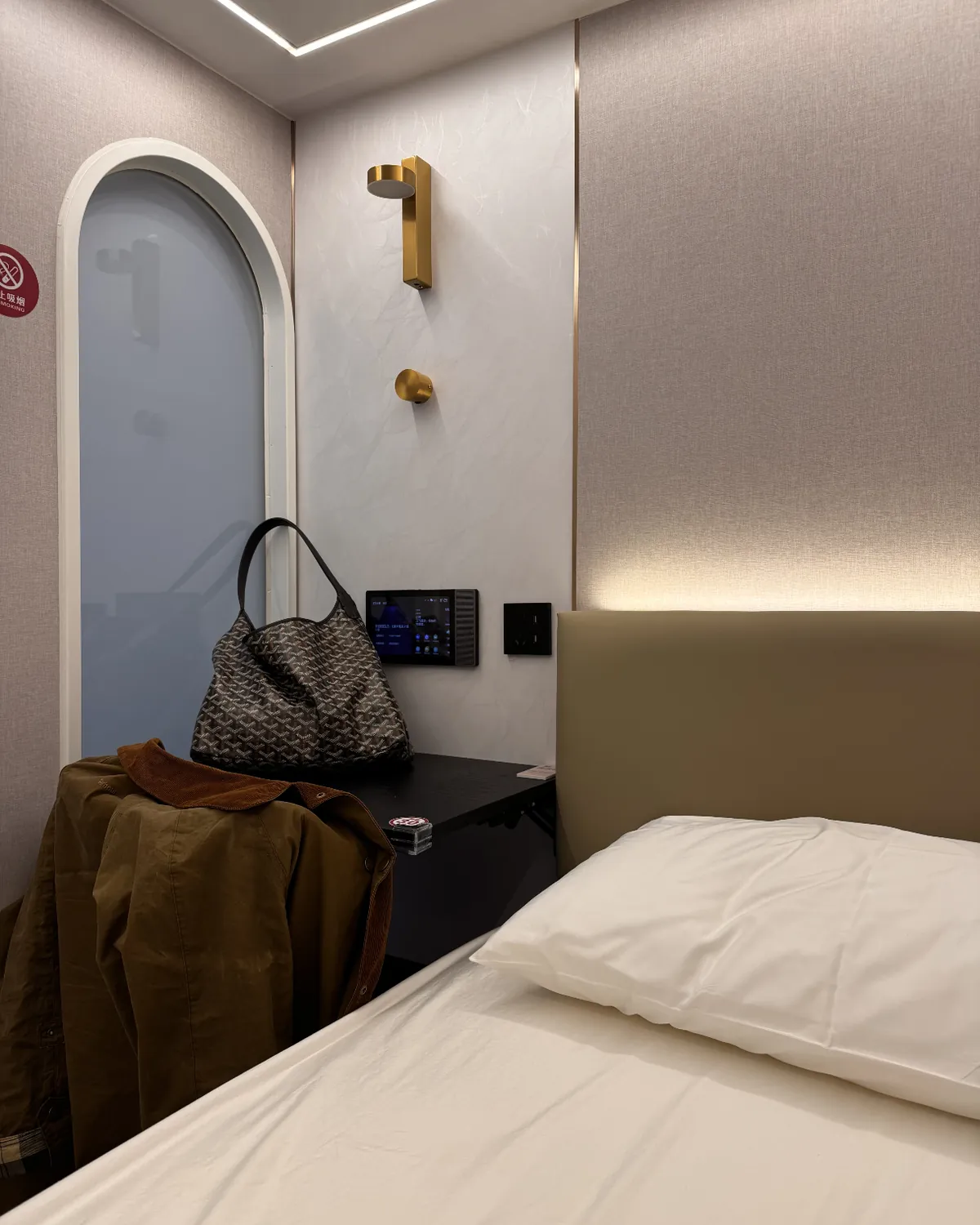 Bed, side table and arched door inside a sleeping pod at Shenzhen airport