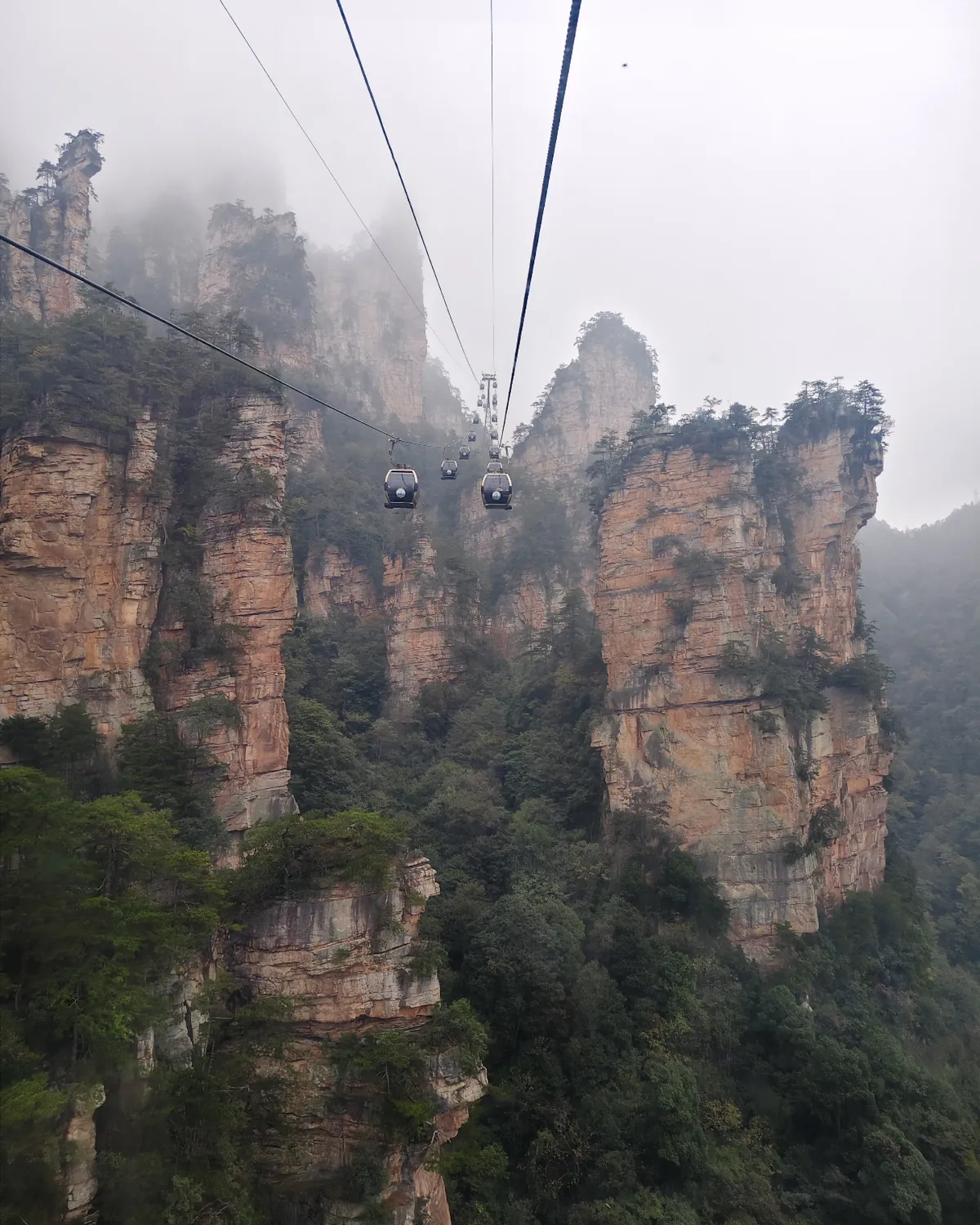 Cable cars travelling between sandstone cliffs in mist in Zhangjiajie